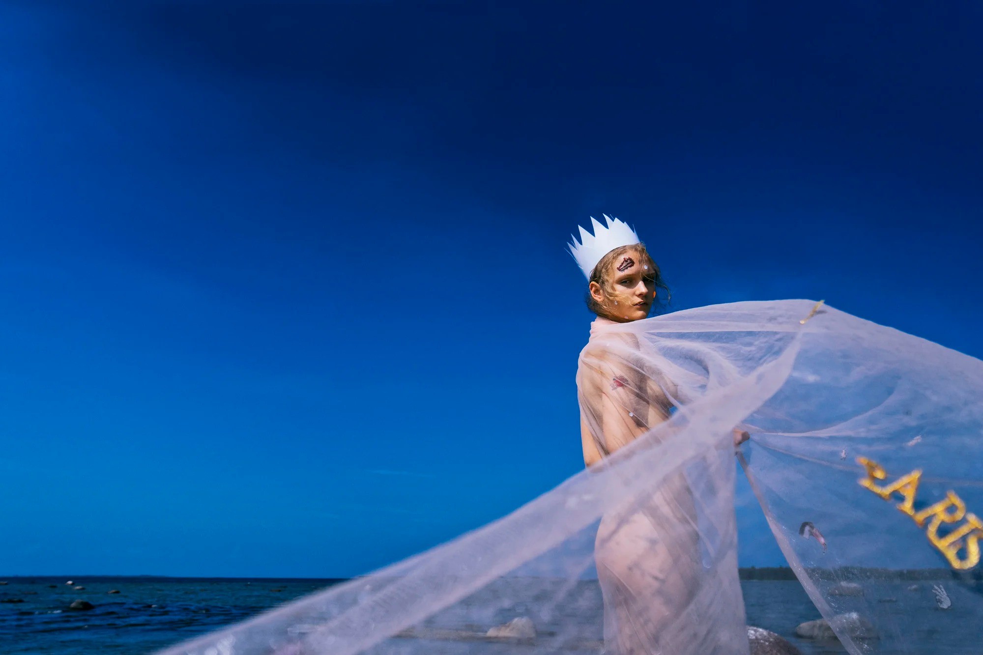 Portrait with a paper crown and flowing pale fabric against a blue sky